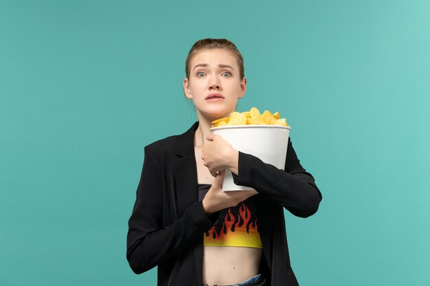 Free photo front view young female holding package with chips and watching movie on light blue surface