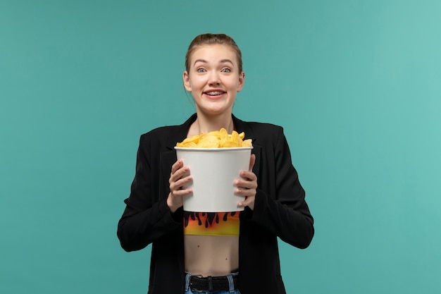 Front view young female holding package with potato chips and watching movie on blue surface