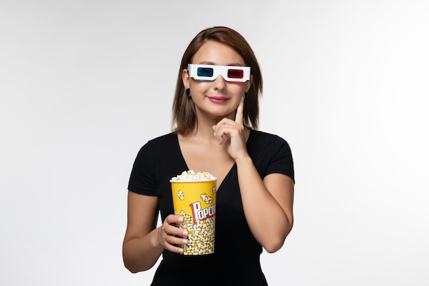 Вид спереди молодая женщина, держащая попкорн в солнцезащитных очках d, смотрит фильм на светлой белой поверхности