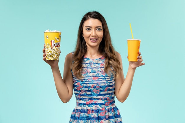 Вид спереди молодая женщина, держащая попкорн и напиток на синей поверхности