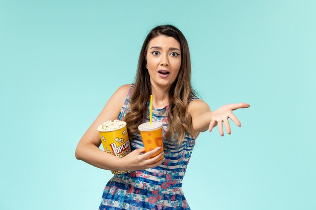 Front view young female holding popcorn and drink on blue surface