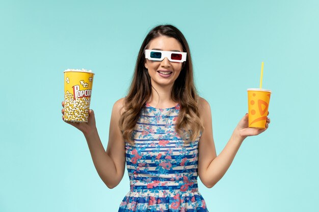 Front view young female holding popcorn drink in d sunglasses on blue surface