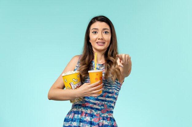 Front view young female holding popcorn and drink on the light blue surface