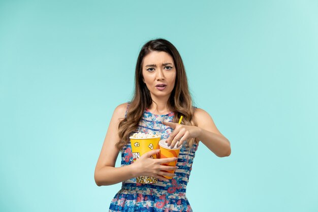 Front view young female holding popcorn and drink watching movie on blue desk