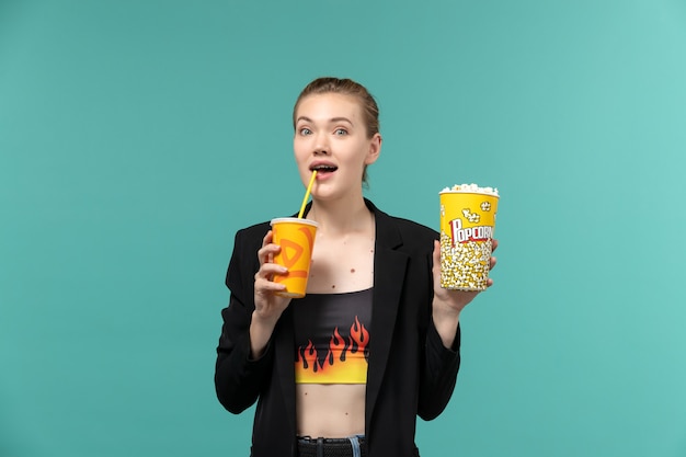 Вид спереди молодая женщина держит попкорн и смотрит фильм на синей поверхности