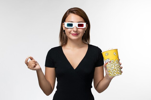 ポップコーンを保持し、白い表面で映画を見ているdサングラスで食べる若い女性