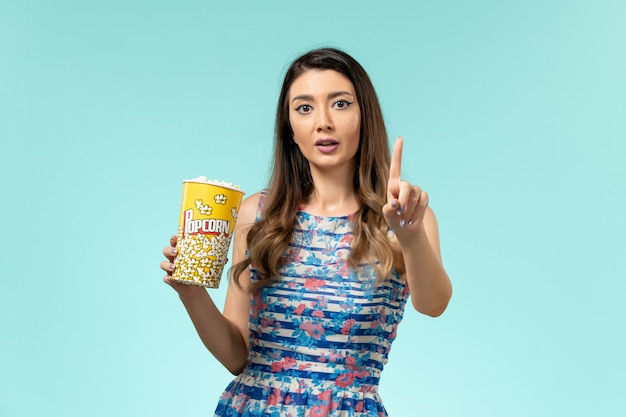 Front view young female holding popcorn package on blue surface