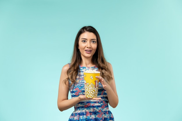 Вид спереди молодая женщина, держащая пакет попкорна на синей поверхности