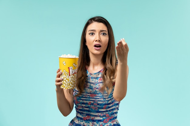 Front view young female holding popcorn package on blue surface