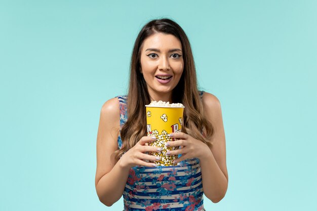 Front view young female holding popcorn package on the blue surface