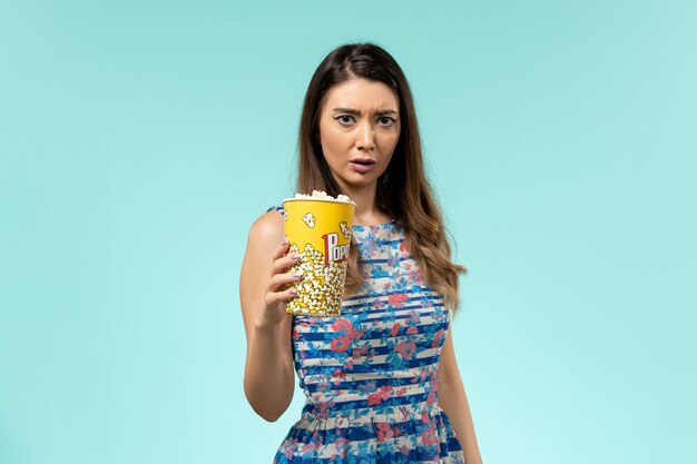 Front view young female holding popcorn package on the blue surface