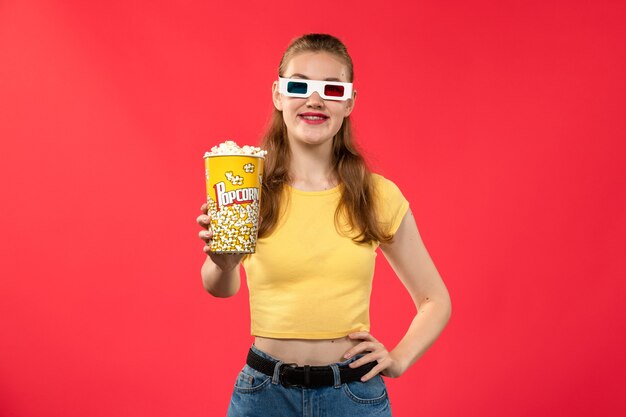 밝은 붉은 벽 극장 영화 시네마 필름에 D 선글라스에 팝콘 패키지를 들고 전면보기 젊은 여성