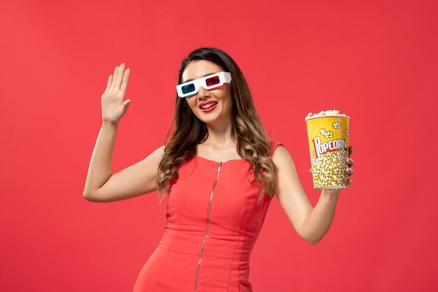 Front view young female holding popcorn package in d sunglasses on red desk