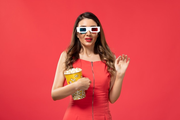 Front view young female holding popcorn package in d sunglasses on the red surface