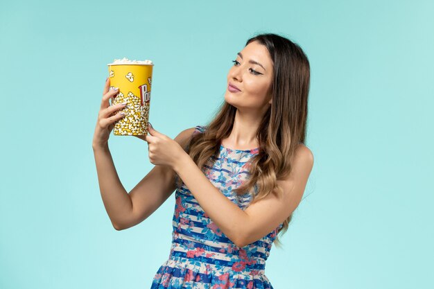 Front view young female holding popcorn package on light-blue surface