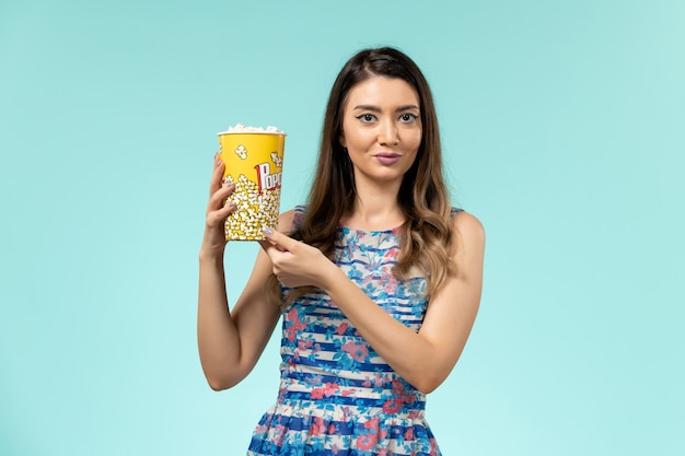 Вид спереди молодая женщина, держащая пакет попкорна на голубой поверхности