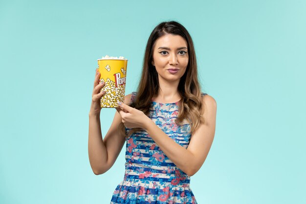 Front view young female holding popcorn package on light blue surface