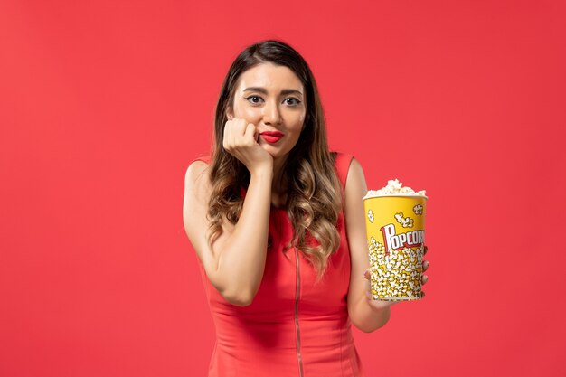 Front view young female holding popcorn package on light red surface