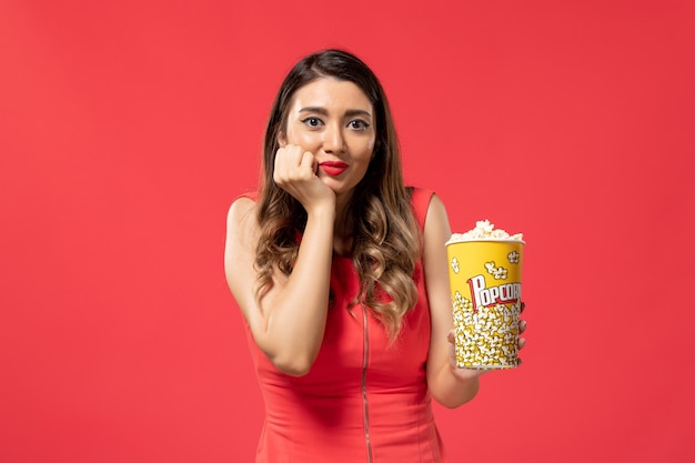 Front view young female holding popcorn package on light red surface