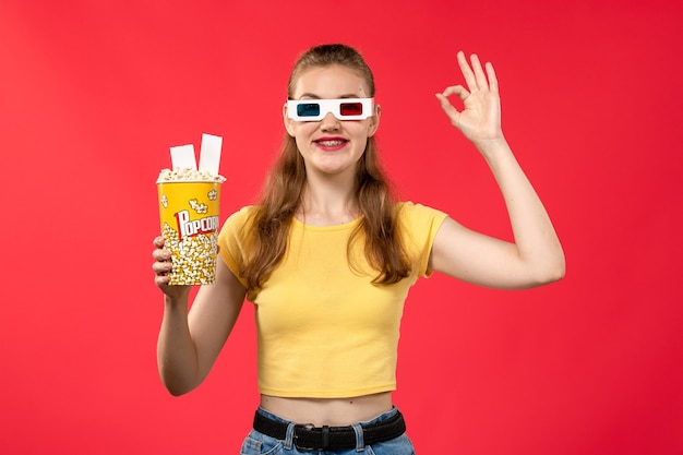 Front view young female holding popcorn package on light red wall theater movie cinema girl film