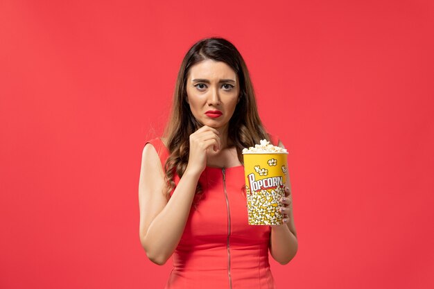 Вид спереди молодая женщина, держащая пакет попкорна, подчеркнула красную поверхность