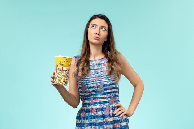 Front view young female holding popcorn package and thinking on blue surface