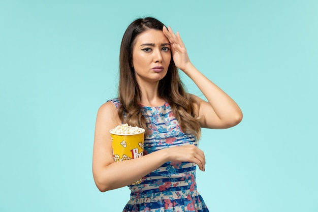 Front view young female holding popcorn package and watching movie on blue surface