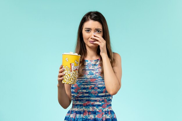 Front view young female holding popcorn package watching movie and crying on blue surface