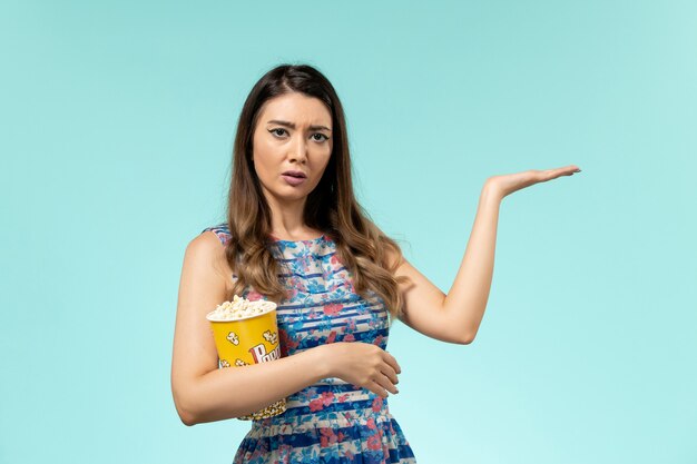 Front view young female holding popcorn package and watching movie on light-blue surface