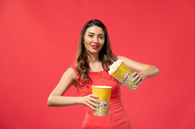 Front view young female holding popcorn packages on light red surface