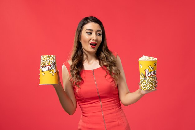 Front view young female holding popcorn packages on red desk