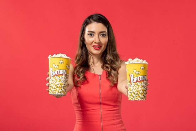 Front view young female holding popcorn packages on red surface