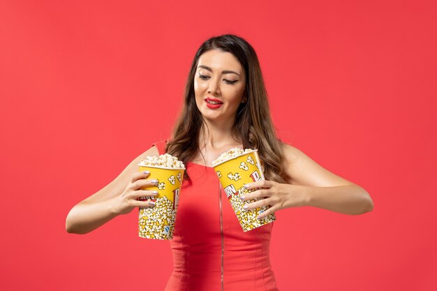 Front view young female holding popcorn packages on the red surface