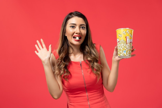 Front view young female holding popcorn on red desk