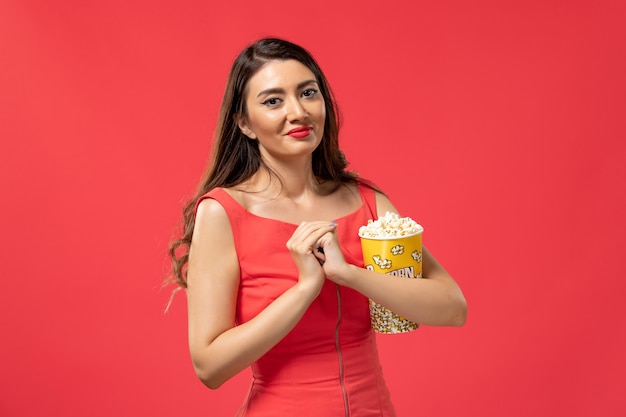 Вид спереди молодая женщина, держащая попкорн на красной поверхности