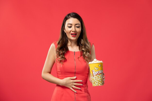 Front view young female holding popcorn on red surface