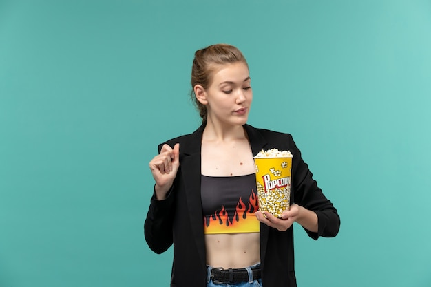 Вид спереди молодая женщина держит попкорн и смотрит фильм на синей поверхности