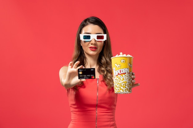 Front view young female holding popcorn with bank card on red surface