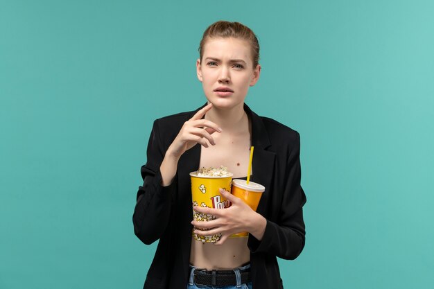 Front view young female holding popcorn with drink and watching movie on blue surface