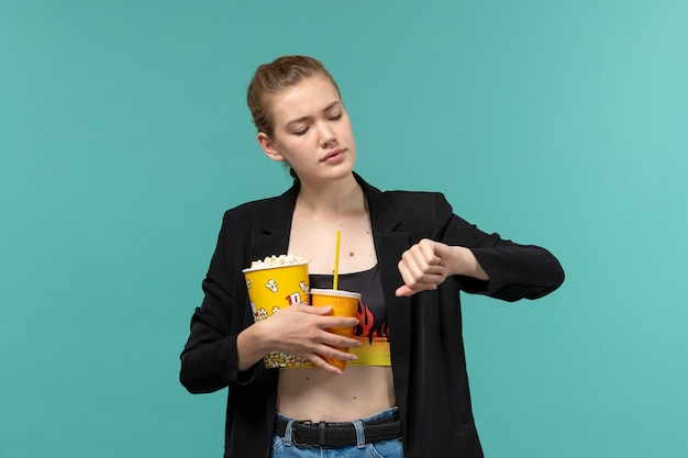 Front view young female holding popcorn with drink and watching movie on the blue surface