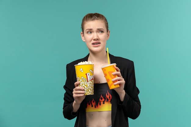 Front view young female holding popcorn with drink and watching movie on the light-blue surface
