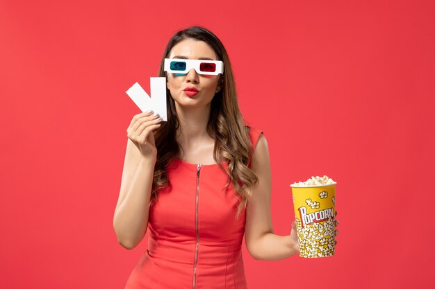 Front view young female holding popcorn with tickets in d sunglasses on light red surface