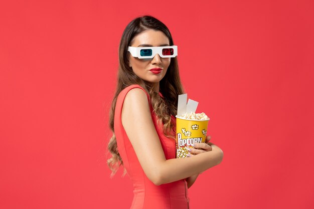Front view young female holding popcorn with tickets in d sunglasses on red surface