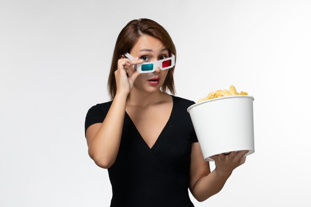 Вид спереди молодая женщина держит картофельные чипсы в солнцезащитных очках d на светло-белой поверхности