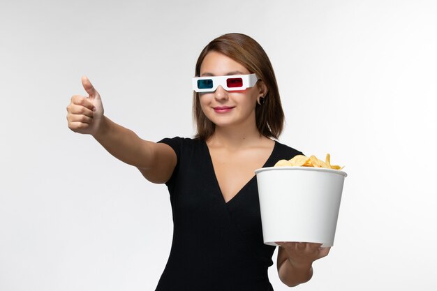Вид спереди молодая женщина держит картофельные чипсы в солнцезащитных очках d и смотрит фильм, улыбаясь на белой поверхности