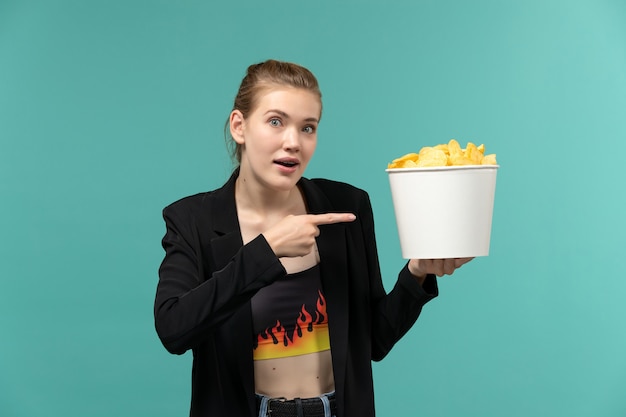 Vista frontale giovane femmina in possesso di patatine fritte e guardare film sulla superficie blu