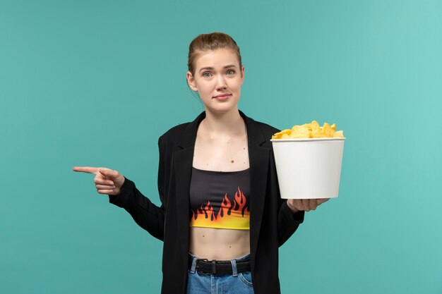 Front view young female holding potato chips and watching movie on the light-blue surface