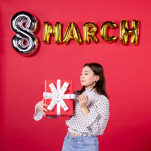 Free photo front view young female holding present on red background woman love holiday beauty equality horizontal march affectionate shopping