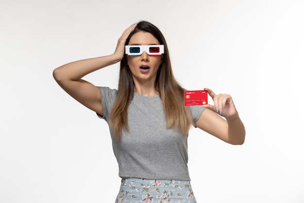 Вид спереди молодая женщина держит красную банковскую карту в солнцезащитных очках d на светлой белой поверхности