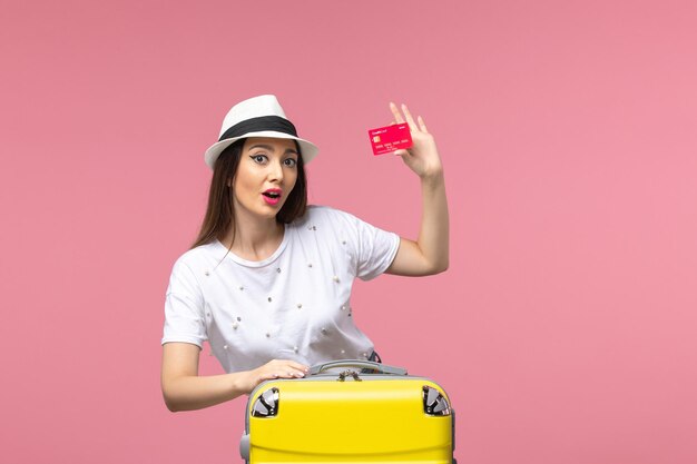 Front view young female holding red bank card on light pink wall color trip summer voyage